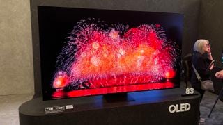 TV Samsung S95F OLED pe un suport gri cu artificii pe ecran