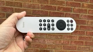 Telecomanda proiectorului home cinema BenQ GV31 ținută în mână în fața unui perete de cărămidă