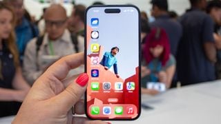 iPhone 16 smartphone ținut în mână, arătând ecranul în fața unei mulțimi de oameni
