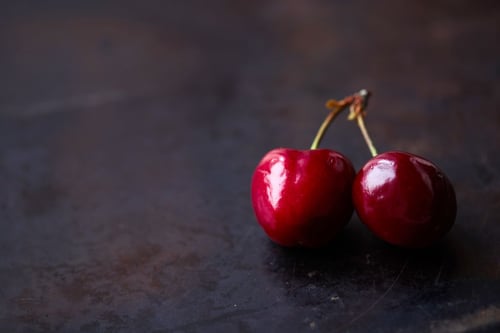a pair of cherries on a dark surface