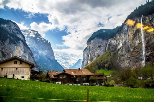 a house in a valley with mountains and snow with Staubbach Falls in the background