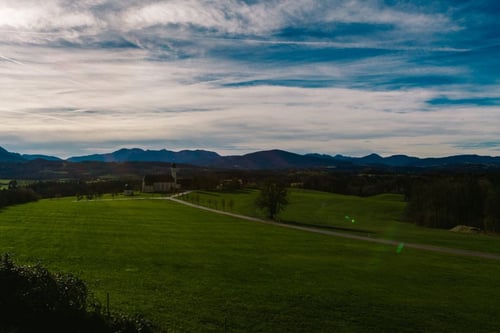 a landscape of a green field with a building and mountains in the background