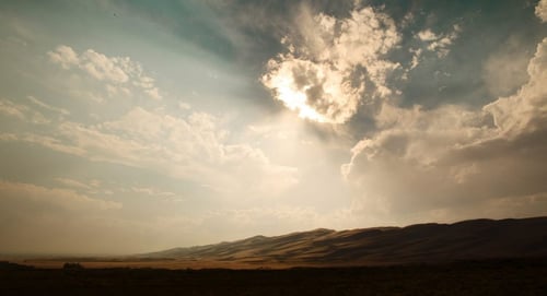 a sun shining through clouds over a desert