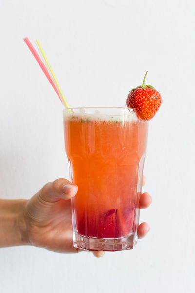 a hand holding a glass of liquid with straws and a strawberry