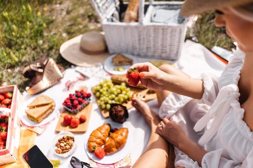 a person holding a strawberry on a picnic blanket