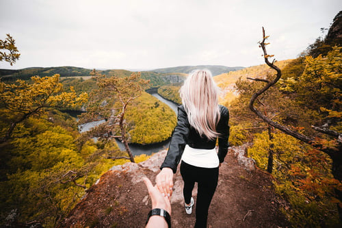 a person holding the hand of a woman walking on a cliff