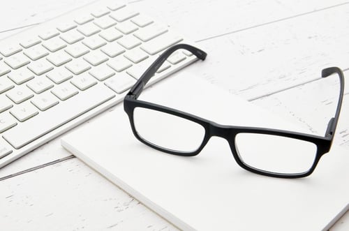 a pair of glasses on a white notebook next to a keyboard