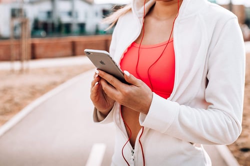 a woman wearing headphones and a white jacket holding a phone