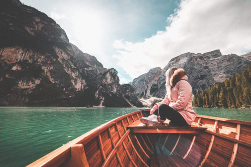 a woman sitting on a boat in a body of water with mountains in the background