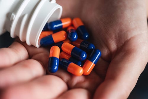 a hand holding a white bottle with blue and orange pills