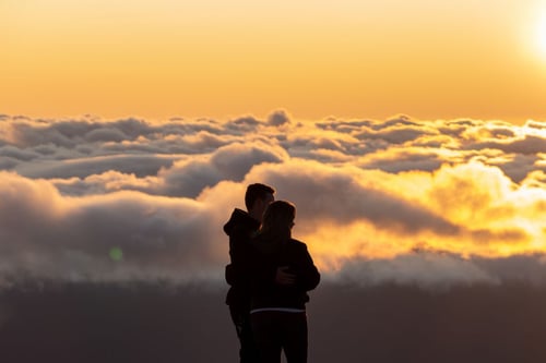 a man and woman standing on a mountain looking at clouds