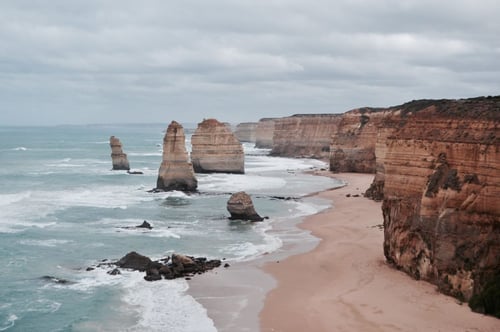 a beach with large rocks and water with The Twelve Apostles in the background