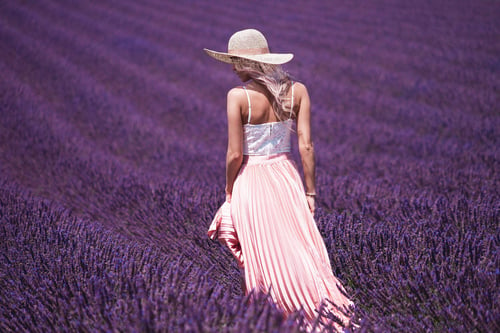 a woman in a hat walking in a field of lavender