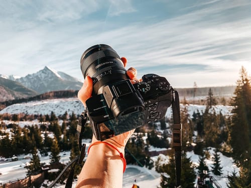 a hand holding a camera with a snowy landscape in the background