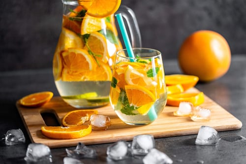 a glass of water with oranges and mint on a cutting board