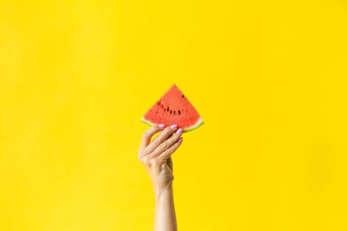 a hand holding a slice of watermelon