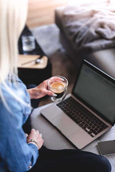 a woman holding a glass of coffee in front of a laptop