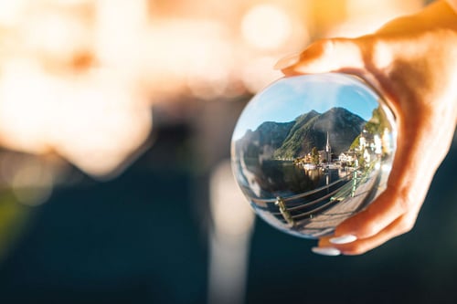 a hand holding a glass ball with a mountain and a city in the background