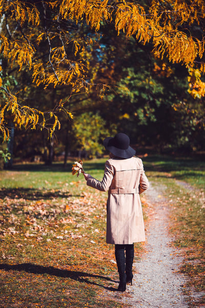 a woman in a hat walking on a path with leaves