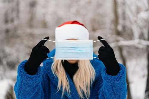 a woman wearing a santa hat and gloves holding a face mask