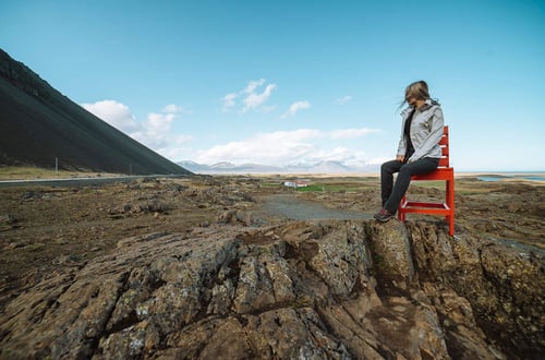 a woman sitting on a red bench in a rocky area