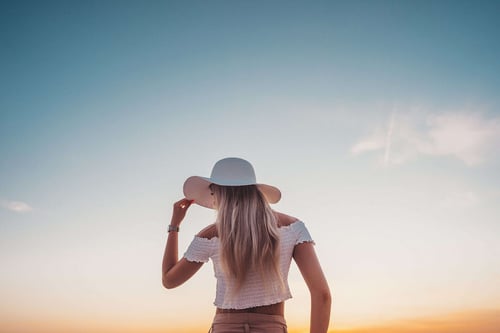 a woman wearing a hat and looking at the sunset
