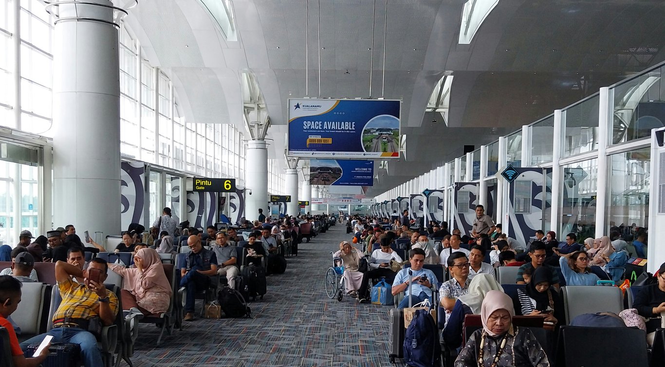 Gate area advertising in out-of-home (OOH) advertising shown with rows of travelers waiting for flights below static banner