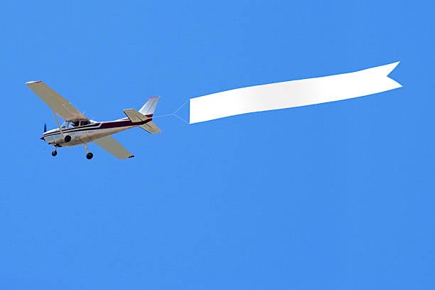 Aerial advertising in out-of-home (OOH) advertising depcited by small plane with white banner in tow
