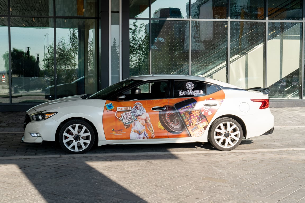 Rideshare advertising shown by white sedan with vehicle wrap ad