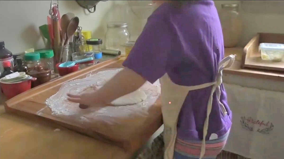 Little girl about 4 years old wearing an apron while rolling out dough on a floured wood bread board