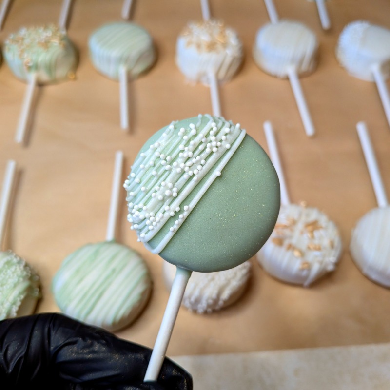 Chocolate cake pop with a light corner drizzle topped with white mini sprinkle dots