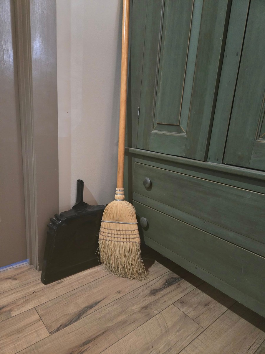 A broom and dustpan quietly sitting in the corner next to an old green cabinet