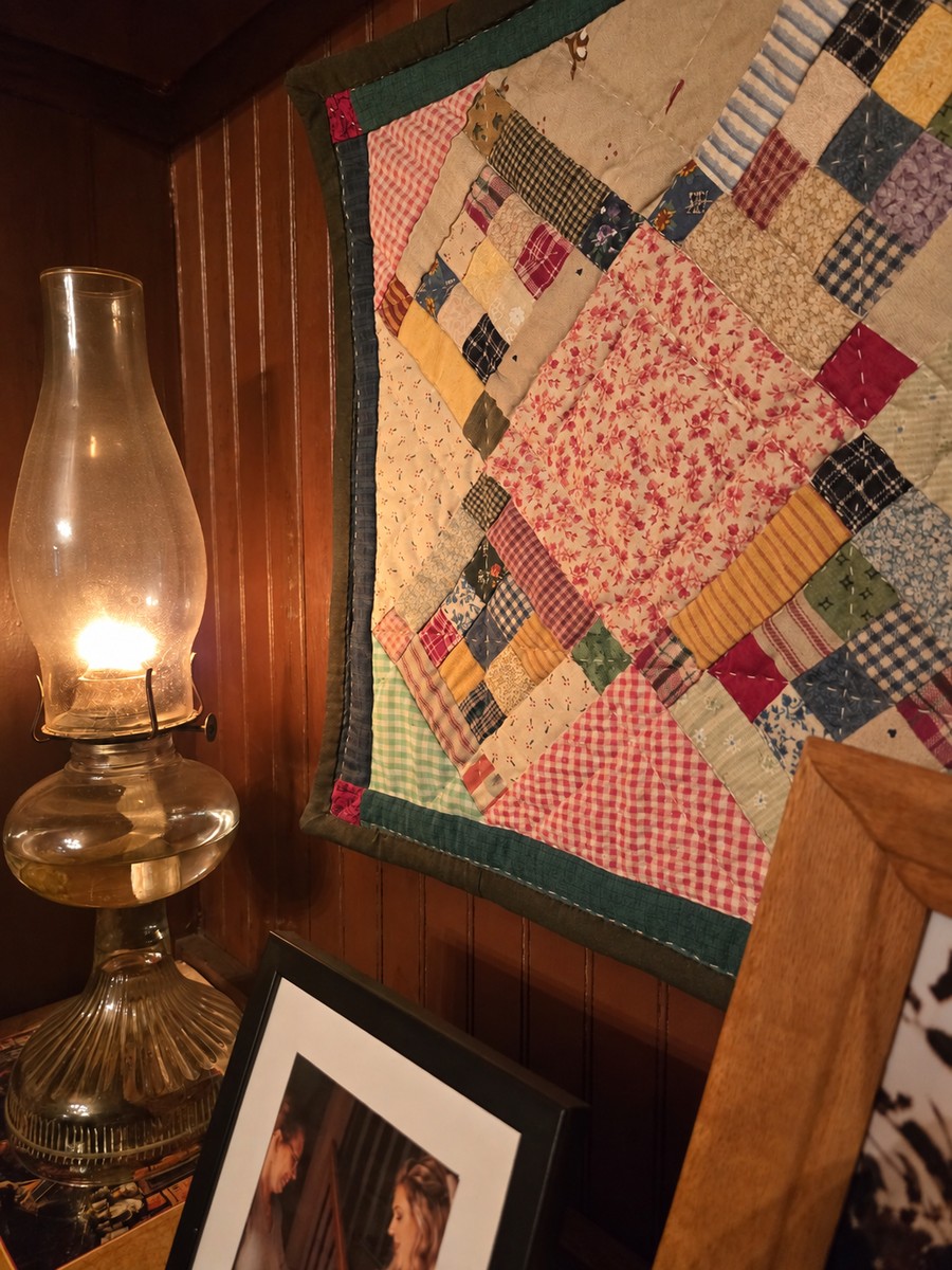 a delicately handstitched quilt hanging on a wall next to the golden glow of a lantern.