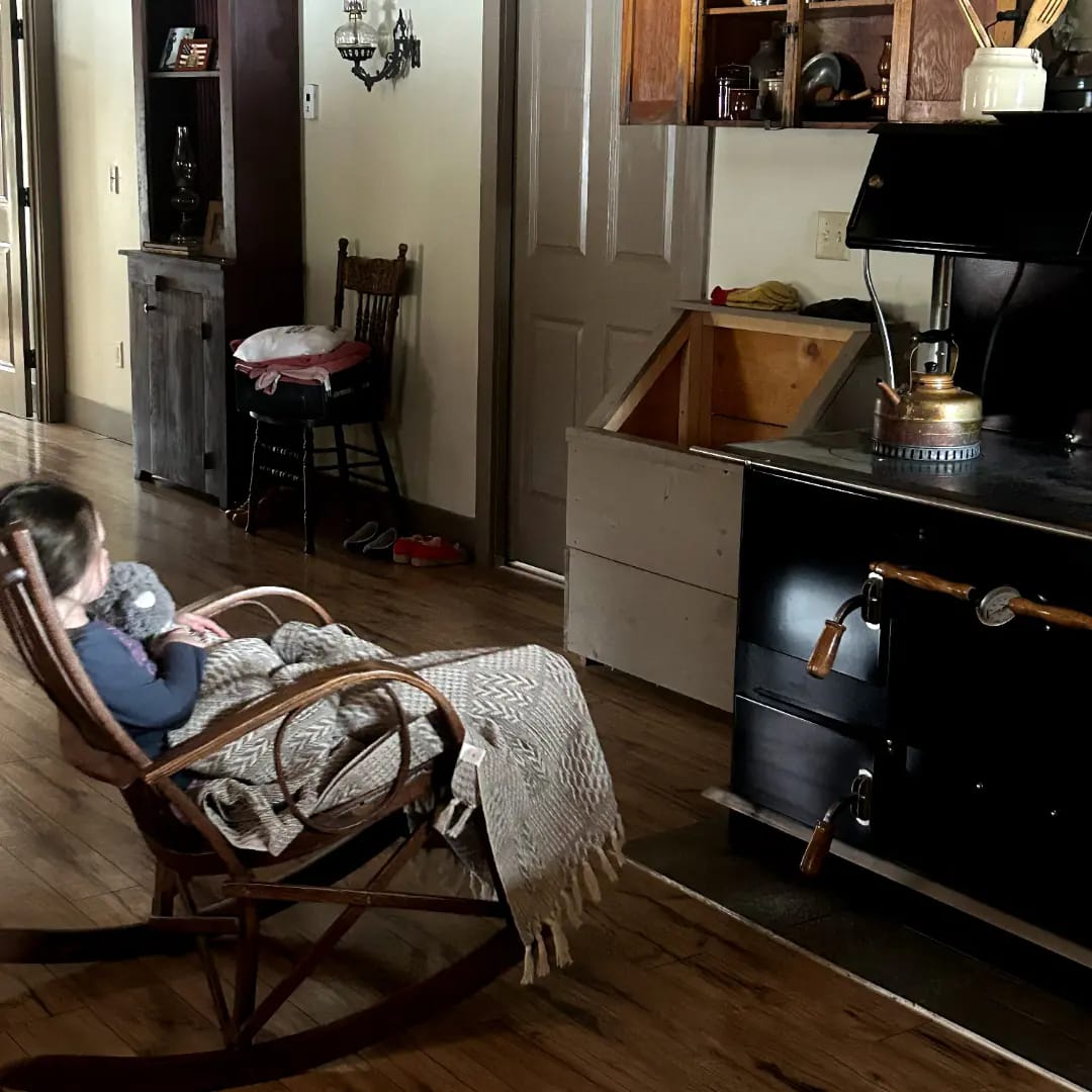 A little girl of 4 years old rocking her blanket wrapped stuffy in front of an old fashioned cook stove