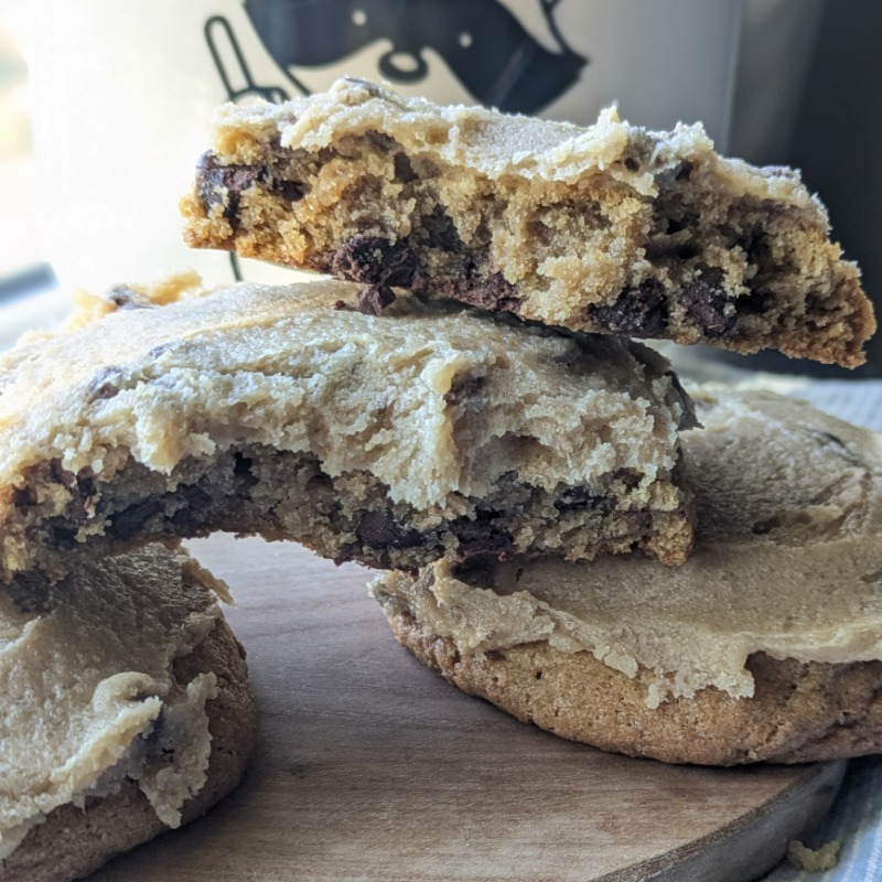 three cookie dough cookies with one broken open layered with cookie dough frosting