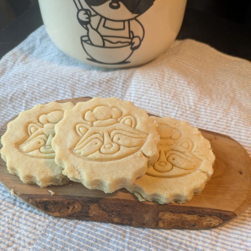 three shortbread with embossed raccoon face on a wooden board