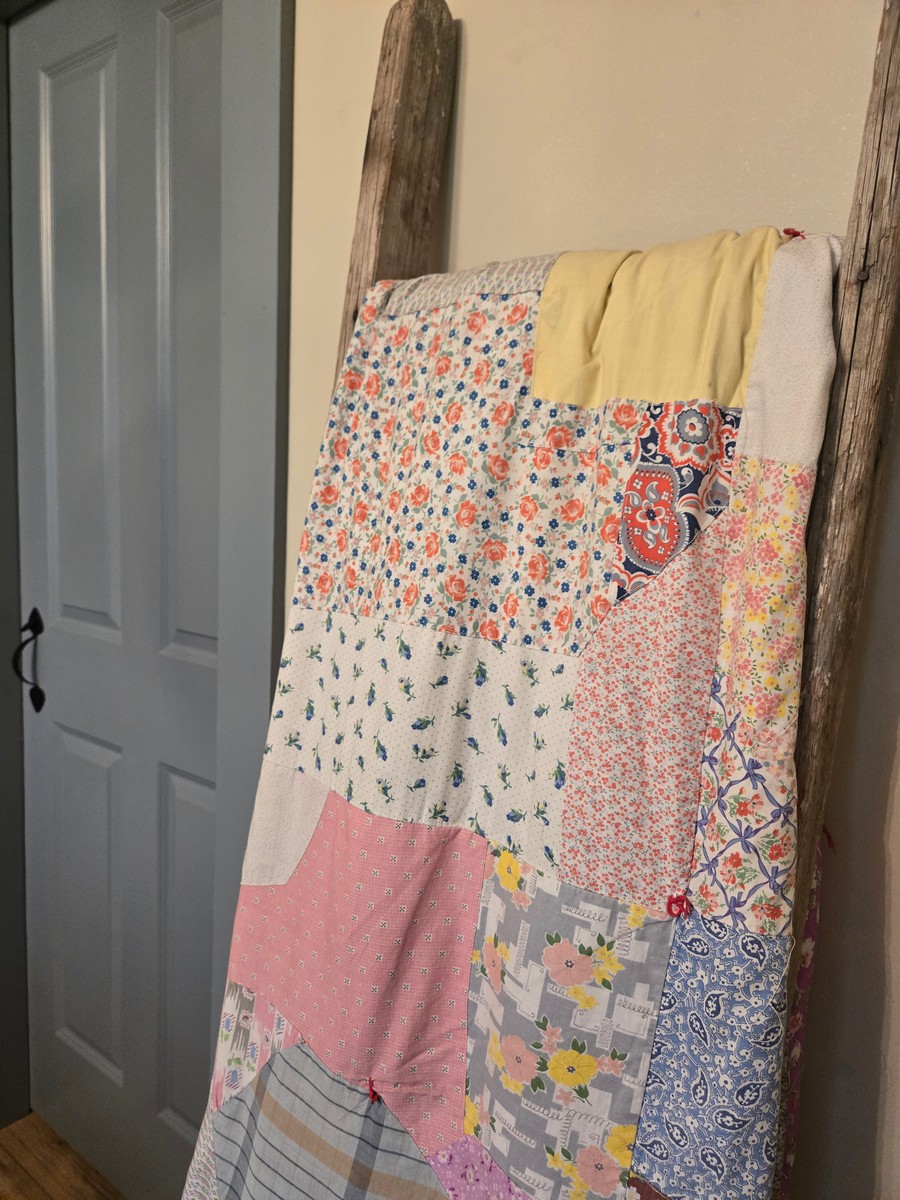 An old quilt in soft colors draped over an old ladder that leans against a bedroom wall.