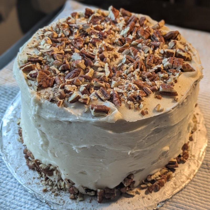 Whole carrot cake with cream cheese frosting, entire top is covered with pecans as well as a ring around the bottom of the cake.