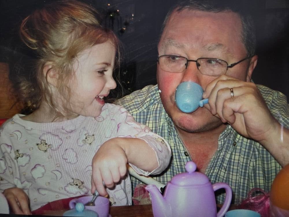 little girl about 4 years old having a tea party with her grandfather. Little girl has a big smile that wrinkles her nose as she watches her grandfather drink tea from a small blue tea cup.