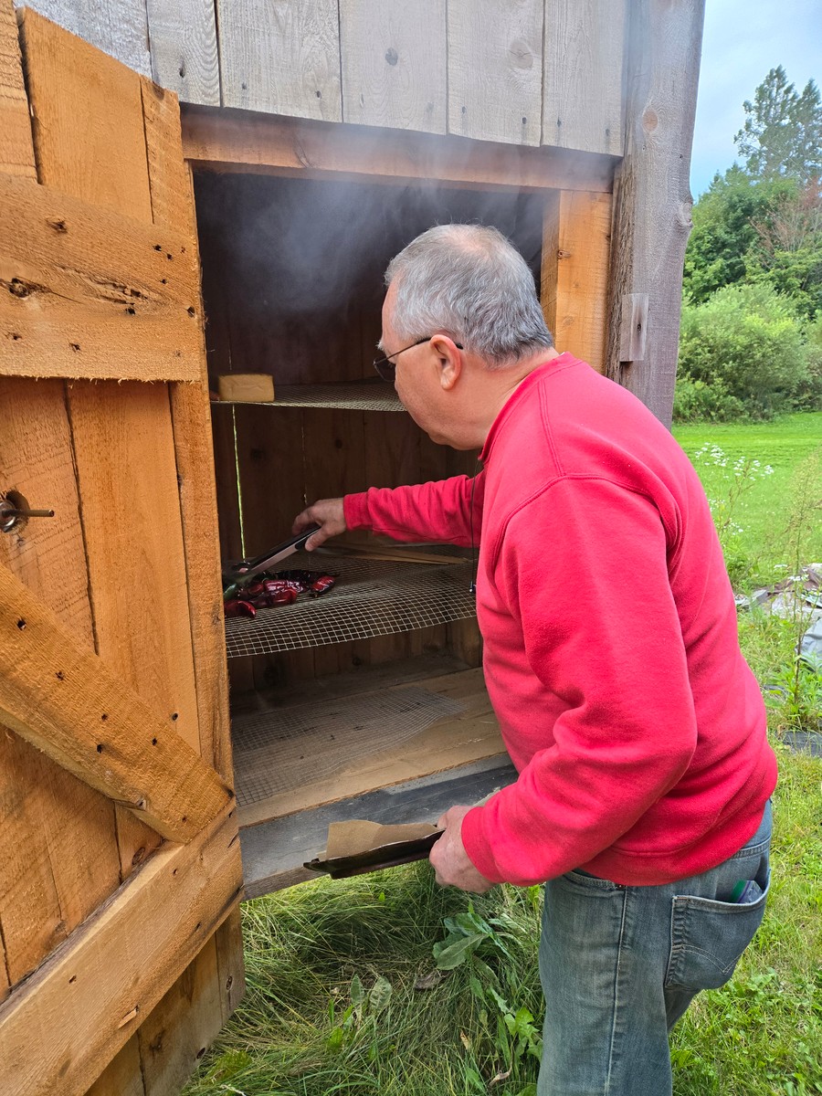 Man in red sweatshirt tending meat and cheese in the smokehouse