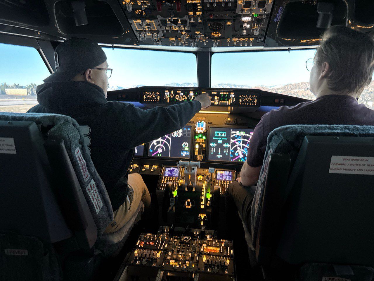Two people sitting in a Boeing 737 MAX flight simulator cockpit
