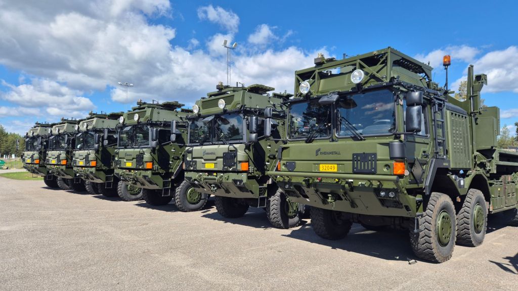 Militära kroklyftlastbilar uppställda utomhus.