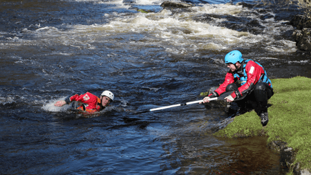 Trainee coach rescuing paddler with paddle.