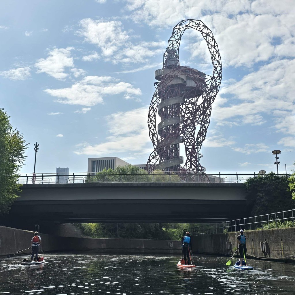 Paddleboarders paddling past the ArcelorMittal Orbit on the Old River Lee