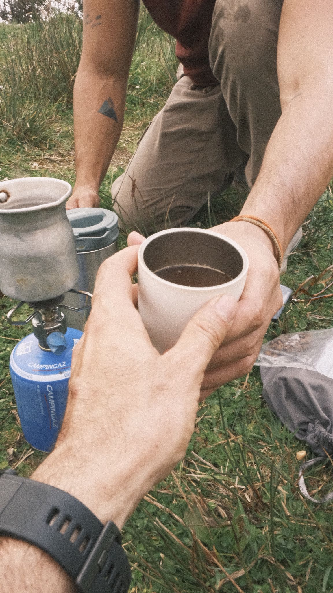 Dos manos se pasan un pocillo de café sobre el pasto