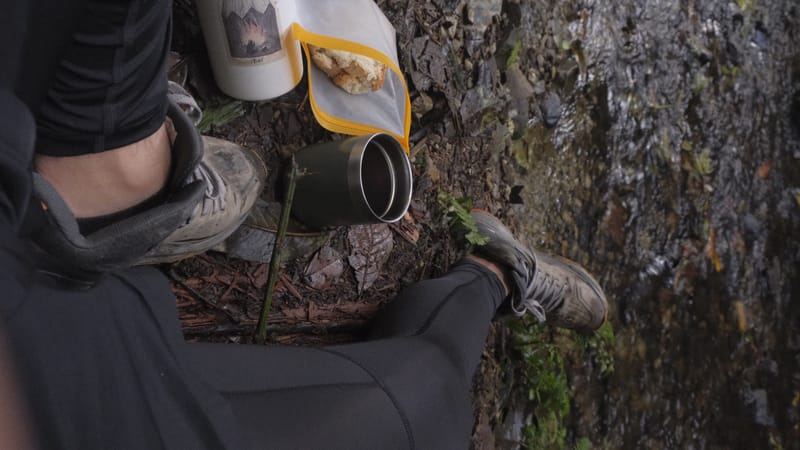 Botas, mochila y un pocillo sobre una roca con musgo