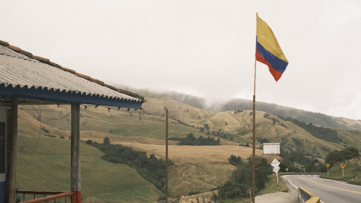Una bandera de Colombia frente a colinas verdes y nubladas