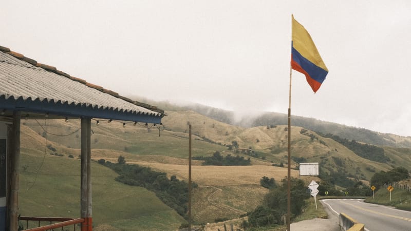 Una bandera de Colombia frente a colinas verdes y nubladas