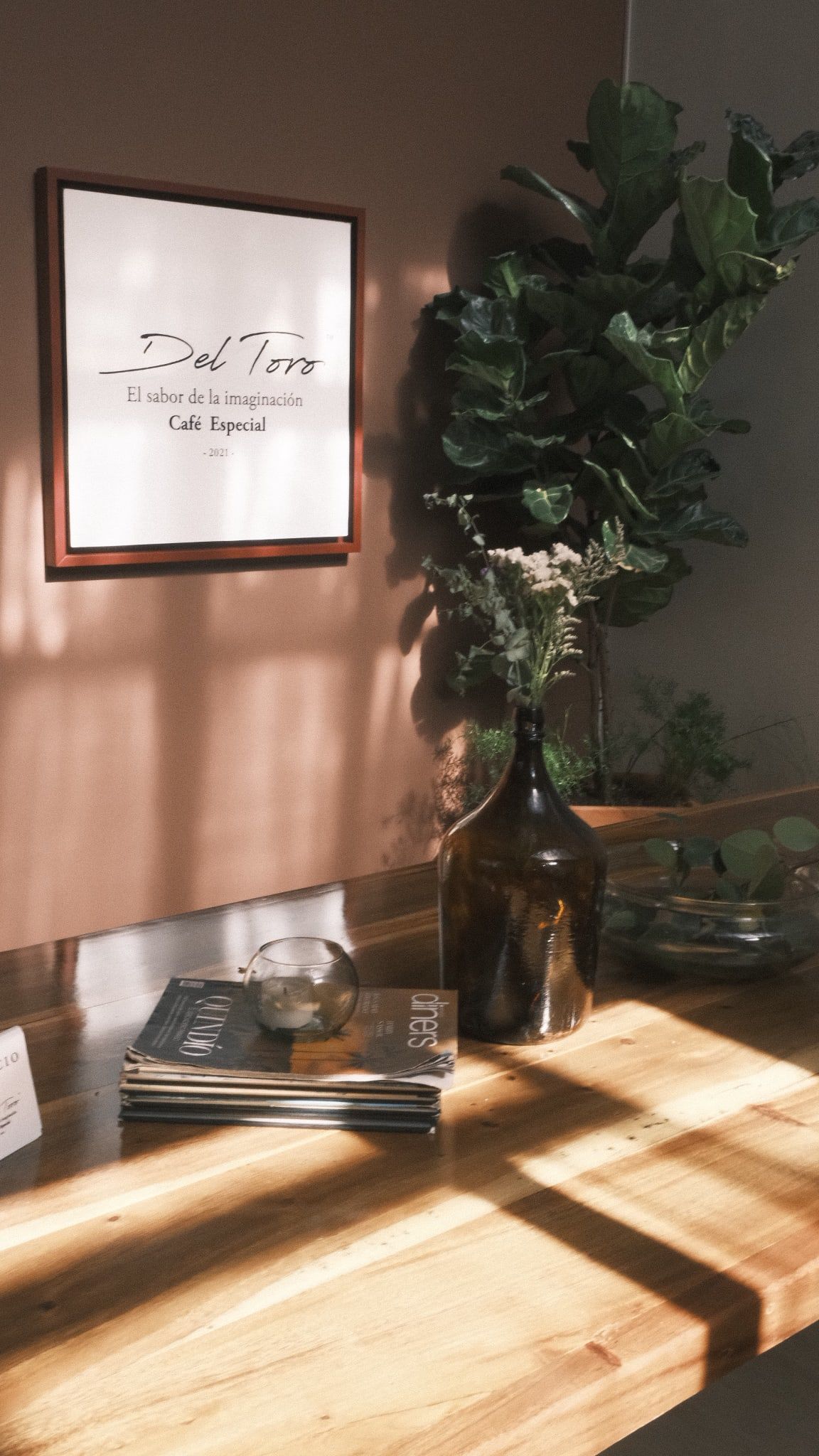 La barra de madera con revistas, una vela y una botella de vidrio ámbar con flores secas, bajo la placa de la casa