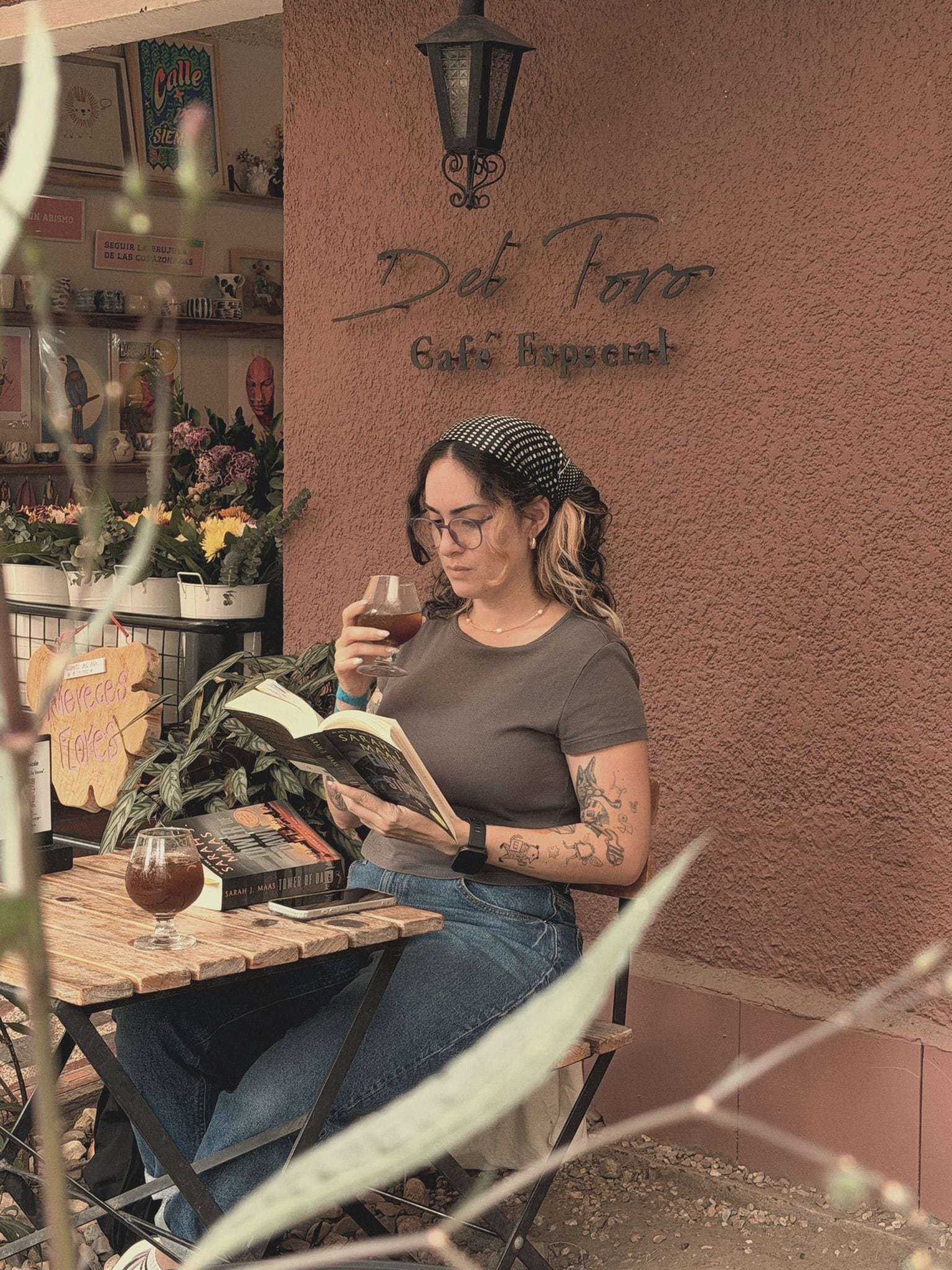 Una mujer lee con una copa de vino en una mesa junto a la fachada, bajo el letrero de la casa